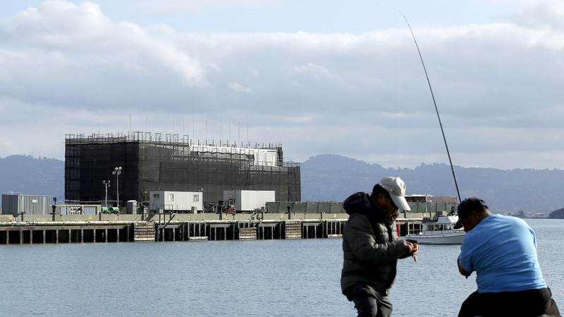 Two men fish in the water in front of a Google barge on Treasure Island in San Francisco. A state agency says Google must move its mystery barge from a construction site on an island in the middle of the San Francisco Bay because the permits are not in order. (AP Photo/Jeff Chiu, File)