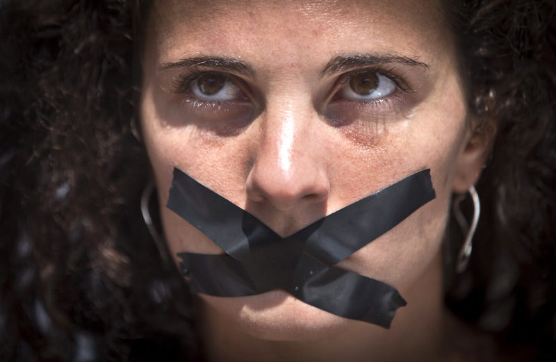 A member of the media sits with black tape across her mouth