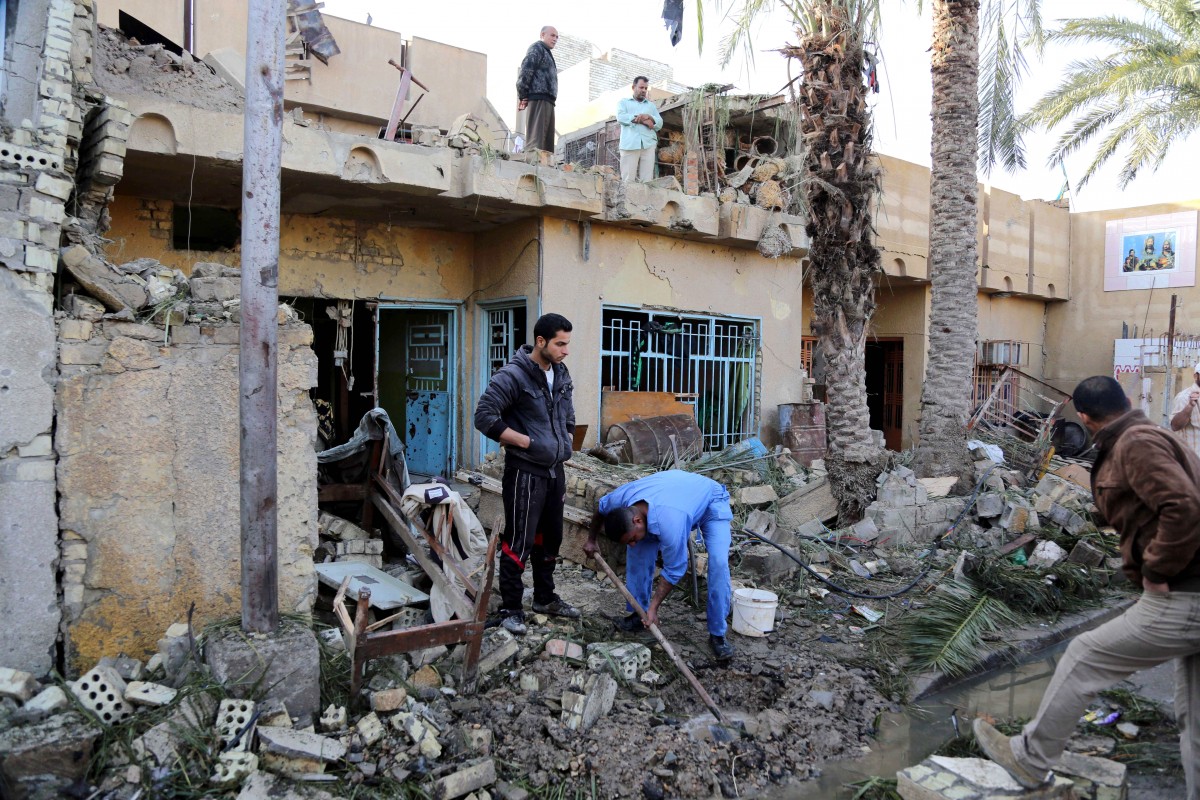 Civilians sift through rubble and stand in the ruins of a home after a car bomb attack in the Shula neighborhood in Baghdad, Iraq