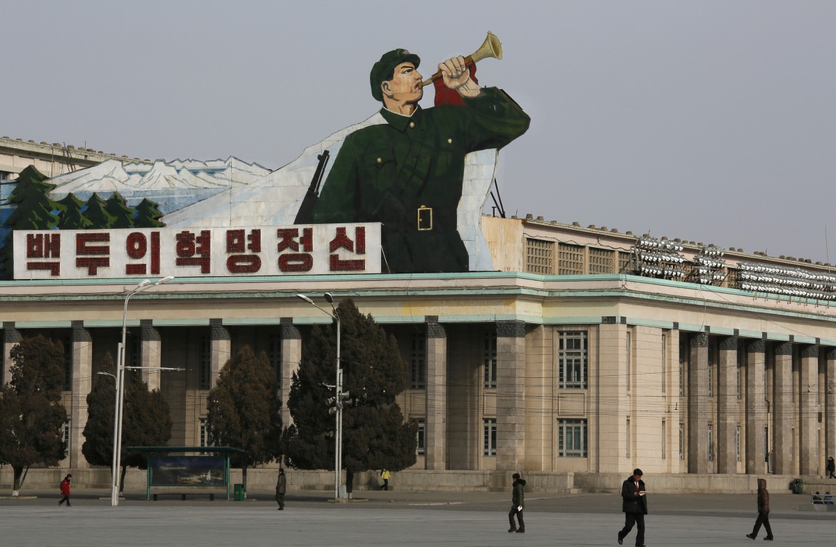 North Korean walk under a sign of a soldier blowing a bugle