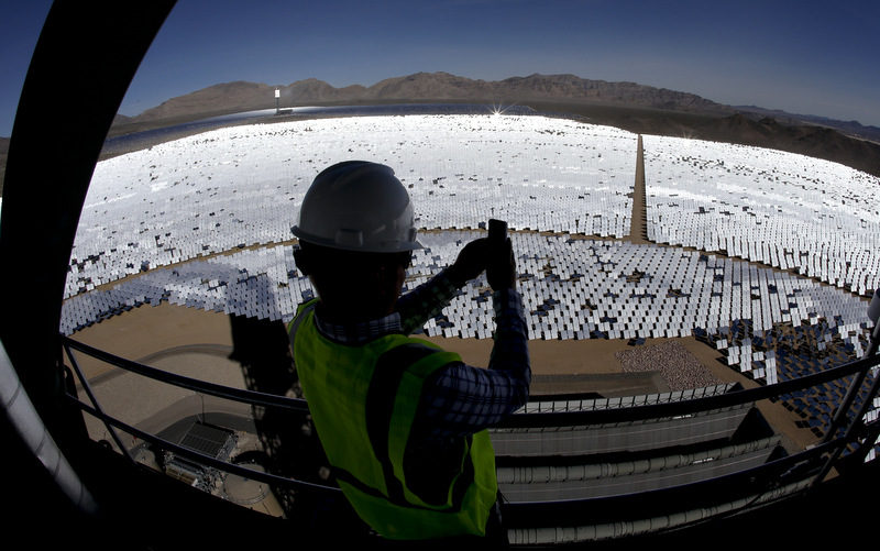 Jeff Holland takes a picture of some of the 300,000 computer-controlled mirrors that reflect sunlight to boilers that sit on 459-foot towers Tuesday, Feb. 11, 2014 in Primm, Nev. The Ivanpah Solar Electric Generating System, sprawling across roughly 5 square miles of federal land near the California-Nevada border, will be opened formally Thursday after years of regulatory and legal tangles. (AP Photo/Chris Carlson)