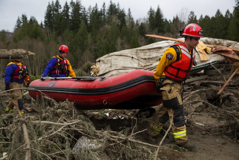 Rescue workers carry an inflatable boat to the flooded area in the debris field caused by the massive mudslide above the North Fork of the Stillaguamish River onto Highway 530, as recovery efforts continue, near Oso, Wash., on Tuesday, March 25, 2014. A scientist working for the government had warned 15 years ago about the potential for a catastrophic landslide in the community where the collapse of a rain-soaked hillside over the weekend killed at least 14 people and left scores missing. (AP Photo/The Seattle Times, Marcus Yam) SEATTLE OUT; USA TODAY OUT; MAGS OUT; TELEVISION OUT; NO SALES; MANDATORY CREDIT TO BOTH THE SEATTLE TIMES AND THE PHOTOGRAPHER