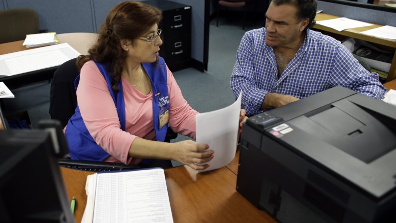 In this Thursday, Feb. 6,  2014 photo, Rose Capote-Marcus, left, helps Waldemar Vega, 50, with problems he is having receiving his unemployment benefits at WorkForce One, in Davie, Fla. On Thursday, Feb. 13, 2014, the Labor Department reports on the number of people who applied for U.S. unemployment benefits a week earlier. (AP Photo/Lynne Sladky)
