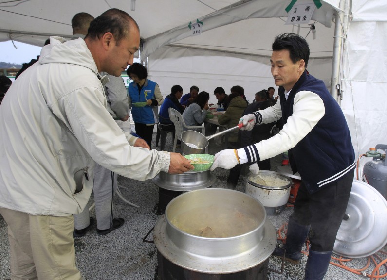 In this April 26, 2014 photo, Lim Jang-young, 58,  volunteer and Japanese restaurant owner, right, ladles out a bowl of traditional beef soup to a relative of a passenger aboard the sunken ferry Sewol in Jindo, South Korea. A sense of national mourning over a tragedy that will likely result in more than 300 deaths, most of them high school students, has prompted an outpouring of volunteers. More than 16,000 people  about half the island's normal population  have come to help.  (AP Photo/Ahn Young-joon)