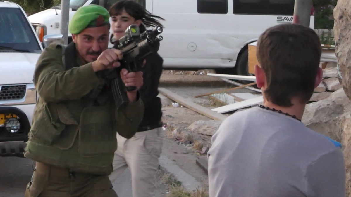 an Israeli soldier points his gun at a Palestinian teen