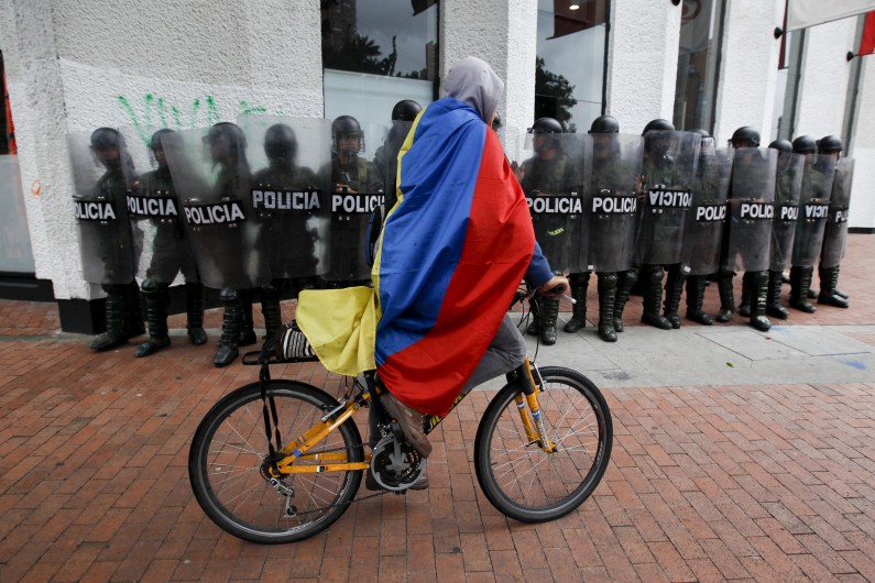 A demonstrator wrapped in a Colombian flag rides past riot police during protests in support of protesting farmers in Bogota, Colombia, Thursday, Aug. 29, 2013. Students marched in support of farmers who have been blockading highways for more than 10 days for an assortment of demands that include reduced gasoline prices, increased subsidies and the cancellation of free trade agreements. (AP Photo/Fernando Vergara)