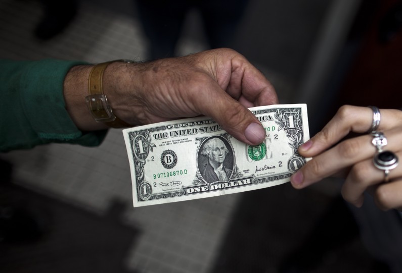 A Liberal Libertario party member offers one dollar at a rate of 5 Argentine pesos to protest against the lack of freedom, such as the right to freely dispose of their own money, in Buenos Aires, Argentina, Monday, May 28, 2012. Argentina is making it harder for people to buy U.S. dollars to pay for travel abroad. A new rule published Monday says anyone wanting to buy dollars for travel must first prove their money was obtained legally, and provide the tax agency with trip details including why, when and where they are traveling. President Cristina Fernandez is cracking down to keep hard currency from flowing out of Argentina, which needs the dollars to maintain its central bank reserves and pay debts. (AP Photo/Natacha Pisarenko)