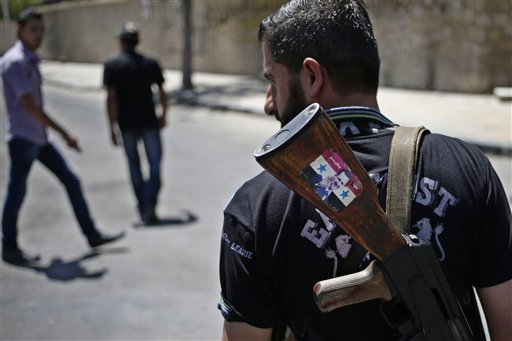 A Syrian military soldier holding his AK-47 with a sticker of Syrian President Bashar Assad and Arabic that reads, "Syria is fine," as he stands guard at a check point in Damascus, Syria. .  (AP Photo/Hassan Ammar, File)