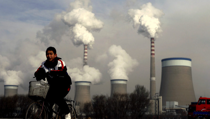 A Chinese boy cycles past a cooling towers of a coal-fired power plant in Dadong, Shanxi province, China.