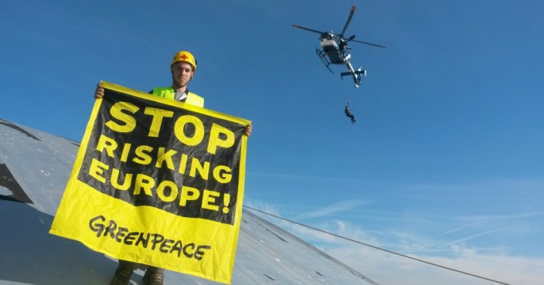 A Greenpeace campaigner holds a banner atop a building at the Fessenheim Nuclear Power Plant in France earlier this year. (Credit: flickr / Greenpeace France)