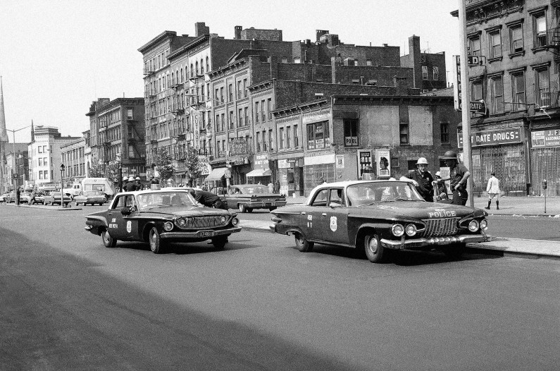 Steel-helmeted police talk with policemen in patrol cars in Lenox Avenue, New York on July 19, 1964 after all night riot in the Harlem section of New York City. Riot developed from rally protesting the killing of a black youth by white policeman in Yorkville on July 16. (AP Photo)
