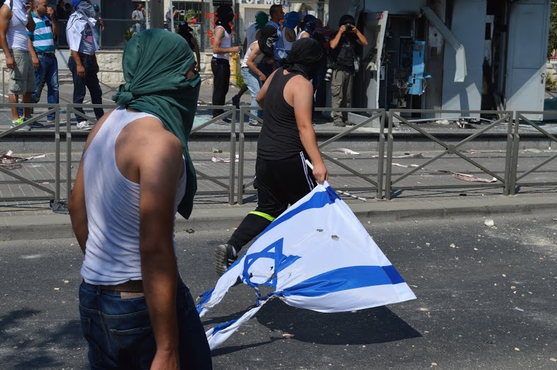 Protesters carry the remains of an Israeli flag along the rubble strewn roads of Shufat. Residents have been protesting against increasing Israeli settler violence and price tag attacks that resulted in the death of Mohammed Abu Khdeir. (Photo by Matthew Vickery for Mint Press)