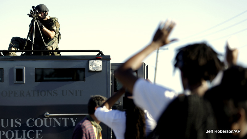 A member of the St. Louis County Police Department points his weapon in the direction of a group of protesters in Ferguson, Mo. on Wednesday, Aug. 13, 2014.