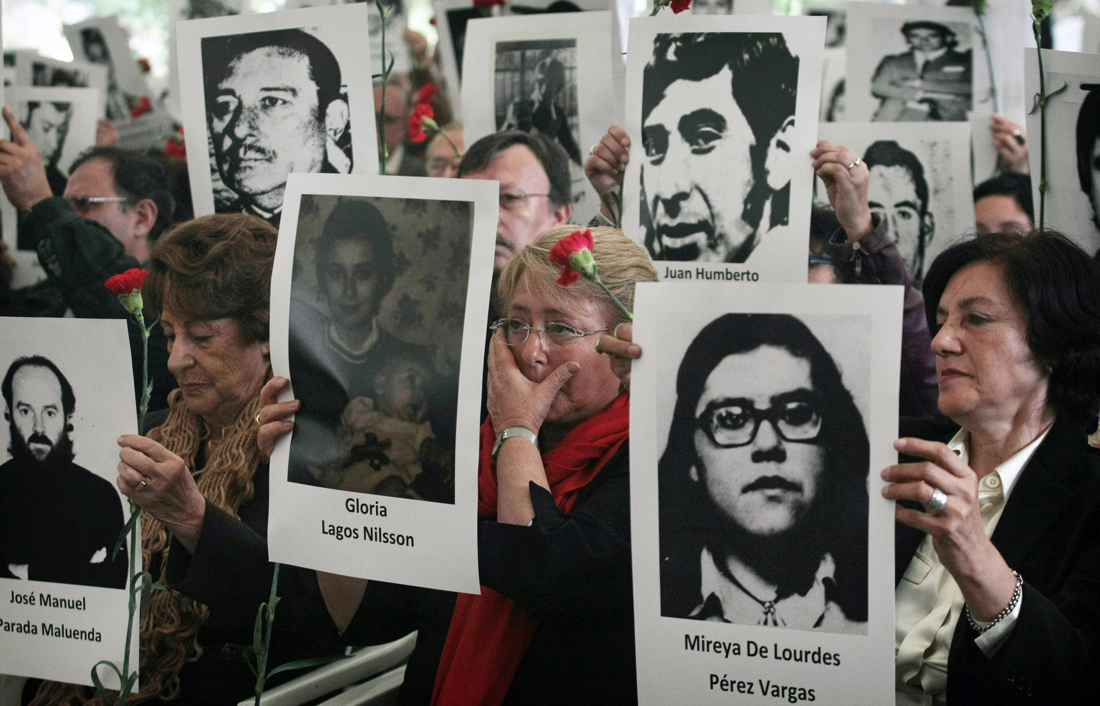 Chile's former President Michelle Bachelet, center, wipes a tear as she stands with her mother Angela Jeria, left, and Margarita Romero, president of the Villa Grimaldi organization, right, all holding photographs of victims of the dictatorship of Gen. Augusto Pinochet, as she attends a ceremony marking the 40th anniversary of his military coup in Santiago, Chile, Sept. 10, 2013. (AP/Luis Hidalgo)