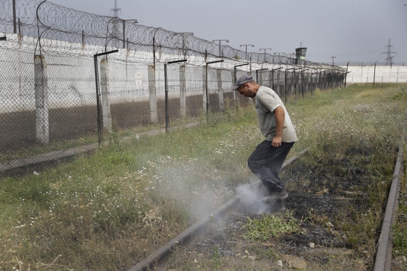 A prisoner tramples smoldering grass in a high-security facility after shelling in Donetsk, eastern Ukraine, Monday, Aug. 11, 2014. Local authorities say more than 100 prisoners have fled from a high-security facility after it was hit by shelling in the rebel stronghold of Donetsk. City council spokesman Maxim Rovensky said Monday a jail riot was precipitated by a direct rocket hit that claimed the life of at least one inmate. The fugitives include people jailed for murder, robbery and rape. (AP Photo/Sergei Grits)