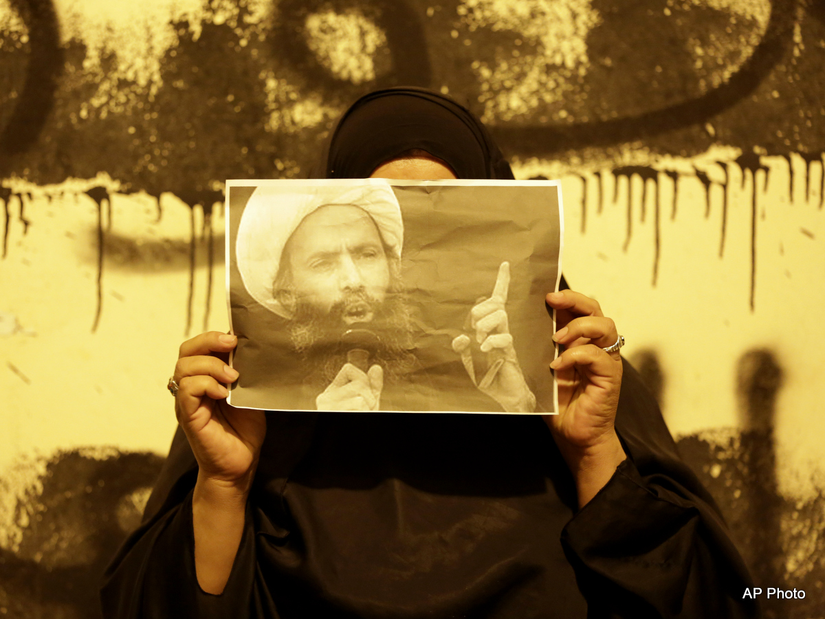 A Bahraini anti-government protester holds up a picture of jailed Saudi Sheik Nimr al-Nimr during clashes between police and protesters in Sanabis, Bahrain, a suburb of the capital Manama, Wednesday night, Oct. 15, 2014. The well-known Shiite cleric was executed January 2, 2016 in Saudi Arabia, sparking fears of renewed unrest from his supporters in the kingdom and neighboring Bahrain. Anti-government graffiti on the wall behind her reads, "We are steadfast and committed to our oath."