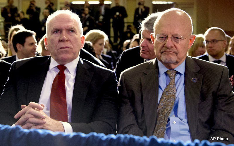 James Clapper, left, and John Brennan, right, sit in the front row of a viewing area, dressed in suits, with many others behind them.