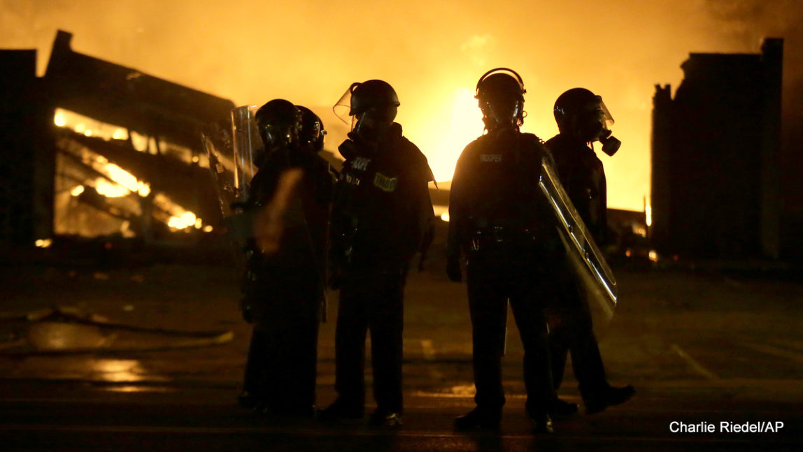 Police officers stand by as buildings are set on fire after the announcement of the grand jury decision, Nov. 24, 2014, in Ferguson, Mo.