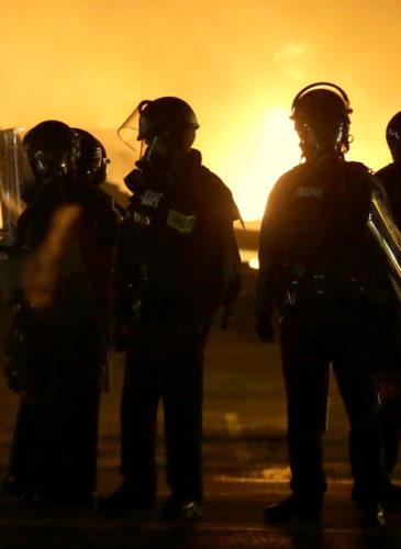 Police officers stand by as buildings are set on fire after the announcement of the grand jury decision, Nov. 24, 2014, in Ferguson, Mo.