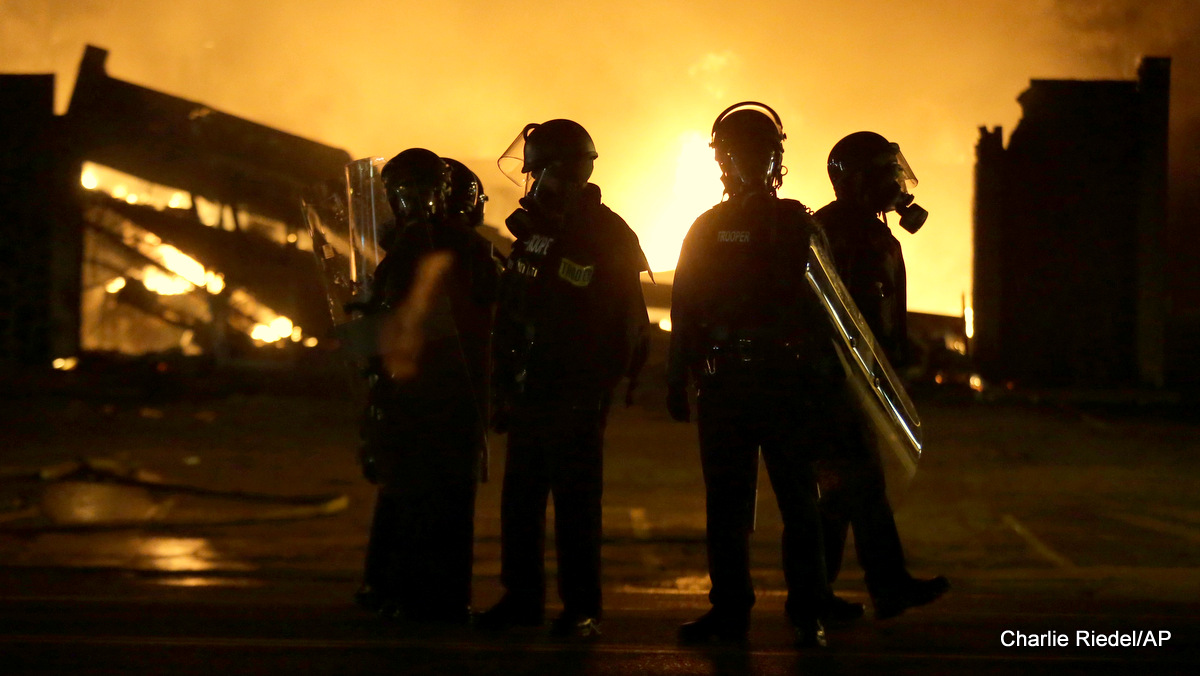 Police officers stand by as buildings are set on fire after the announcement of the grand jury decision, Nov. 24, 2014, in Ferguson, Mo.