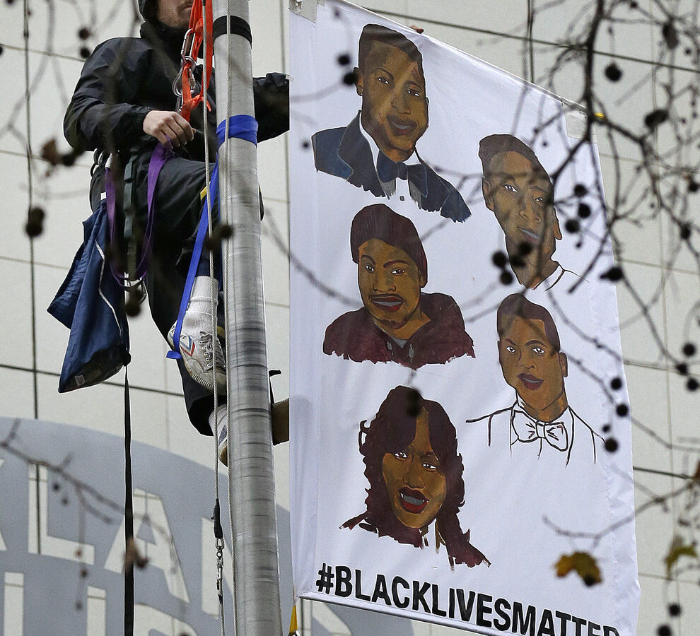 A protestor hangs a banner atop the flagpole of the Oakland Police Department