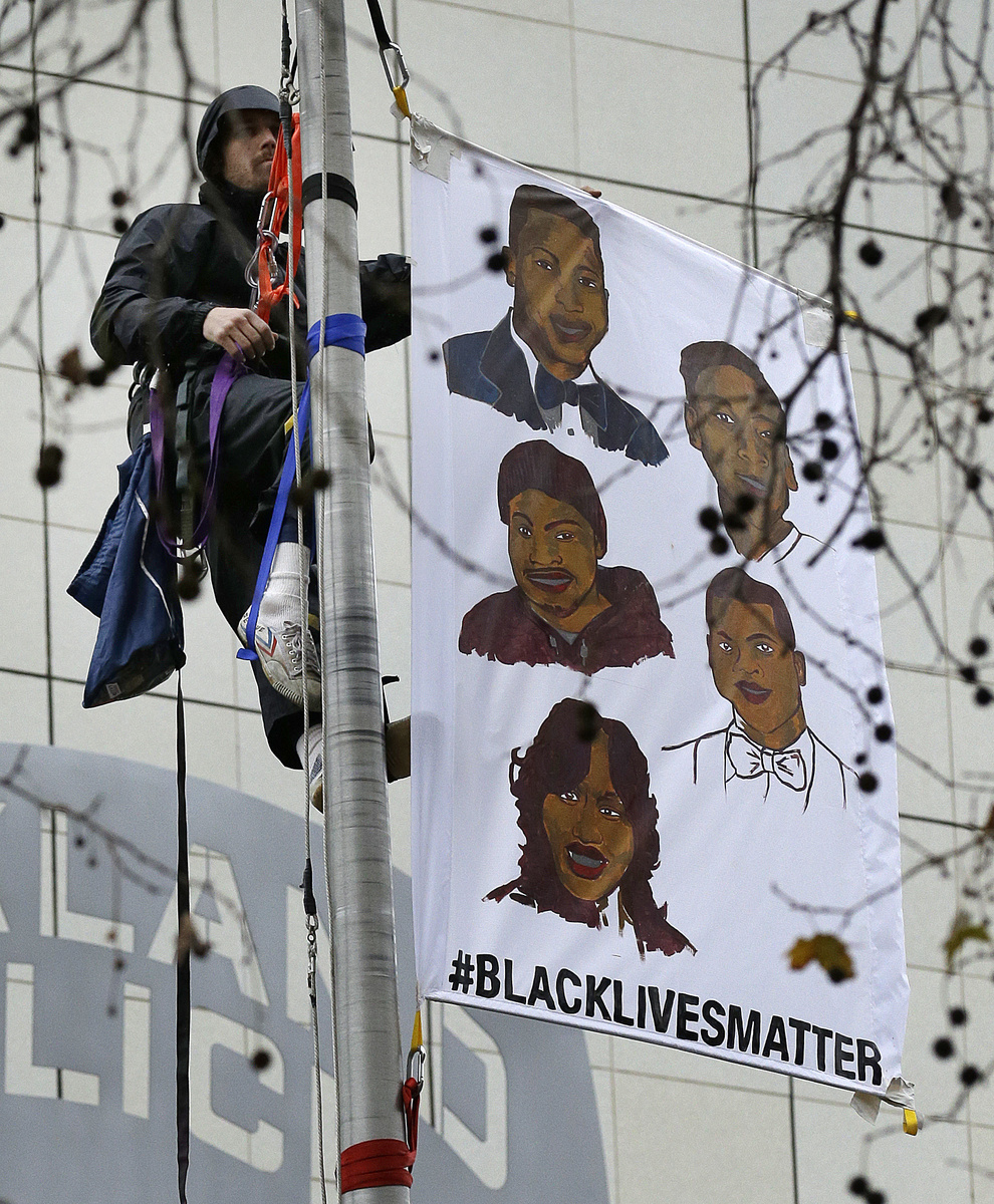 A protestor hangs a banner atop the flagpole of the Oakland Police Department