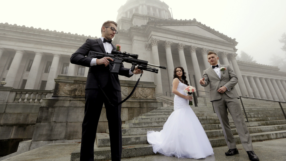 The best man in a wedding party, who all declined to be identified, holds an AR-10 rifle he was handed while the party was having their pre-wedding portraits taken on the steps of the capitol before a rally nearby by gun-rights advocates to protest a new expanded gun background check law in Washington state