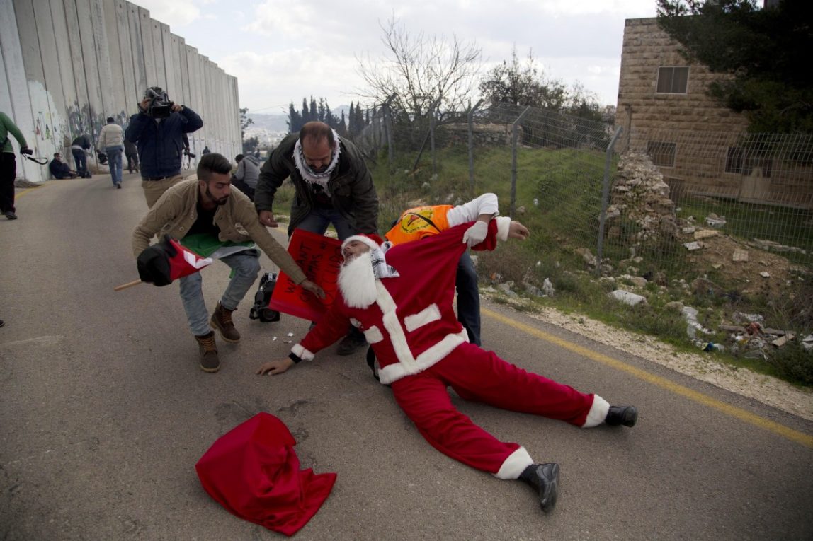 The man in the Santa suit lays prostrate, dragged by medics, his hat fallen off to the side.