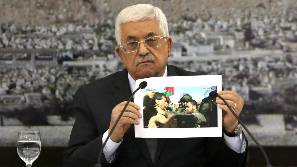 Palestinian President Mahmoud Abbas holds a picture of an Israeli soldier pushing Palestinian Cabinet minister Ziad Abu Ein, Ramallah, Dec. 10, 2014.