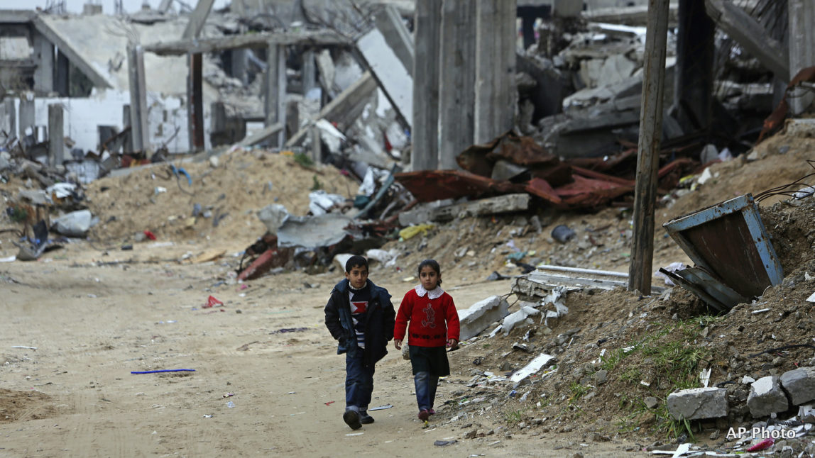 A Palestinian brother and sister walk in front of a building which was destroyed in last summer's Israel-Hamas war, in the Shijaiyah neighborhood of Gaza City, northern Gaza Strip, Monday, Feb. 23, 2015. (AP Photo/Adel Hana)