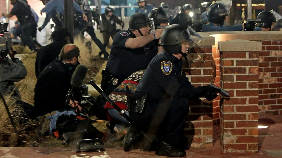 Police take cover after two officers were shot while standing guard in front of the Ferguson Police Station