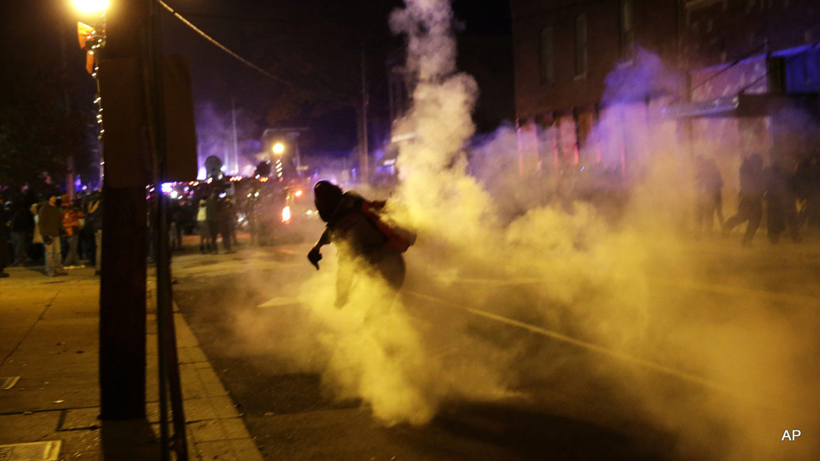 A protester returns a tear gas canister fired by police into the crowd outside of the Ferguson city hall, Tuesday, Nov. 25, 2014, in Ferguson, Mo. Missouri's governor ordered hundreds more state militia into Ferguson on Tuesday, after a night of protests and rioting over a grand jury's decision not to indict police officer Darren Wilson in the fatal shooting of Michael Brown, a case that has inflamed racial tensions in the U.S. (AP Photo/David Goldman)