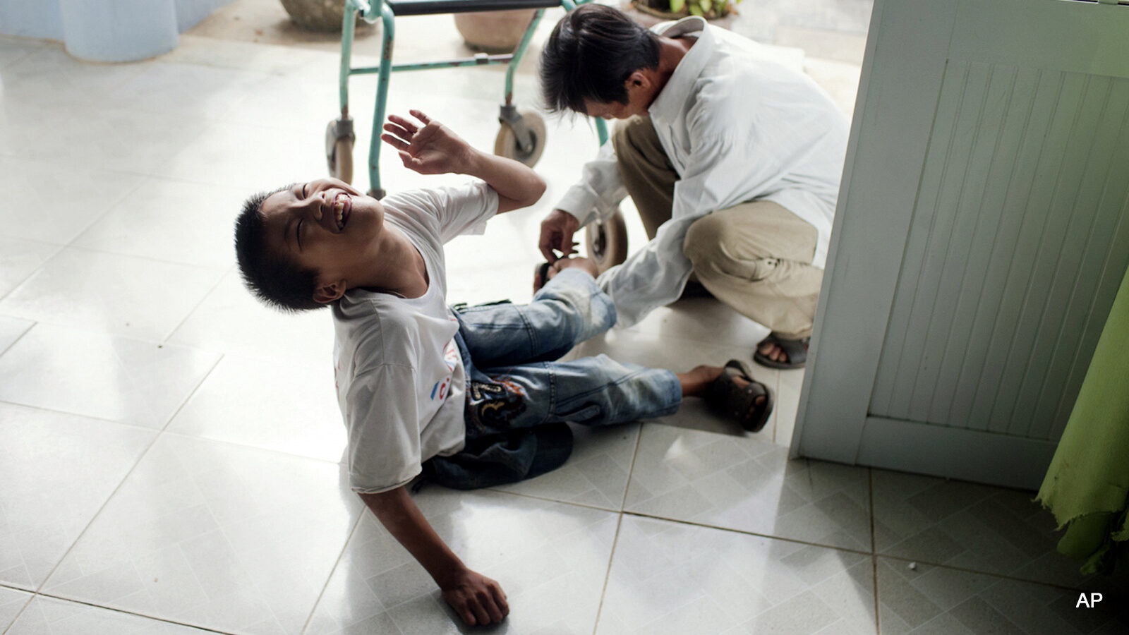 In this photo taken on Wednesday, Aug. 8, 2012, Le Van Tam, 14, is picked up by his father at a rehabilitation center in Danang, Vietnam. The children were born with physical and mental disabilities that the center's director says were caused by their parents' exposure to the chemical dioxin in the defoliant Agent Orange. On Thursday, the U.S. for the first time will begin cleaning up leftover dioxin that was stored at the former military base that's now part of Danang's airport. (AP Photo/Maika Elan)