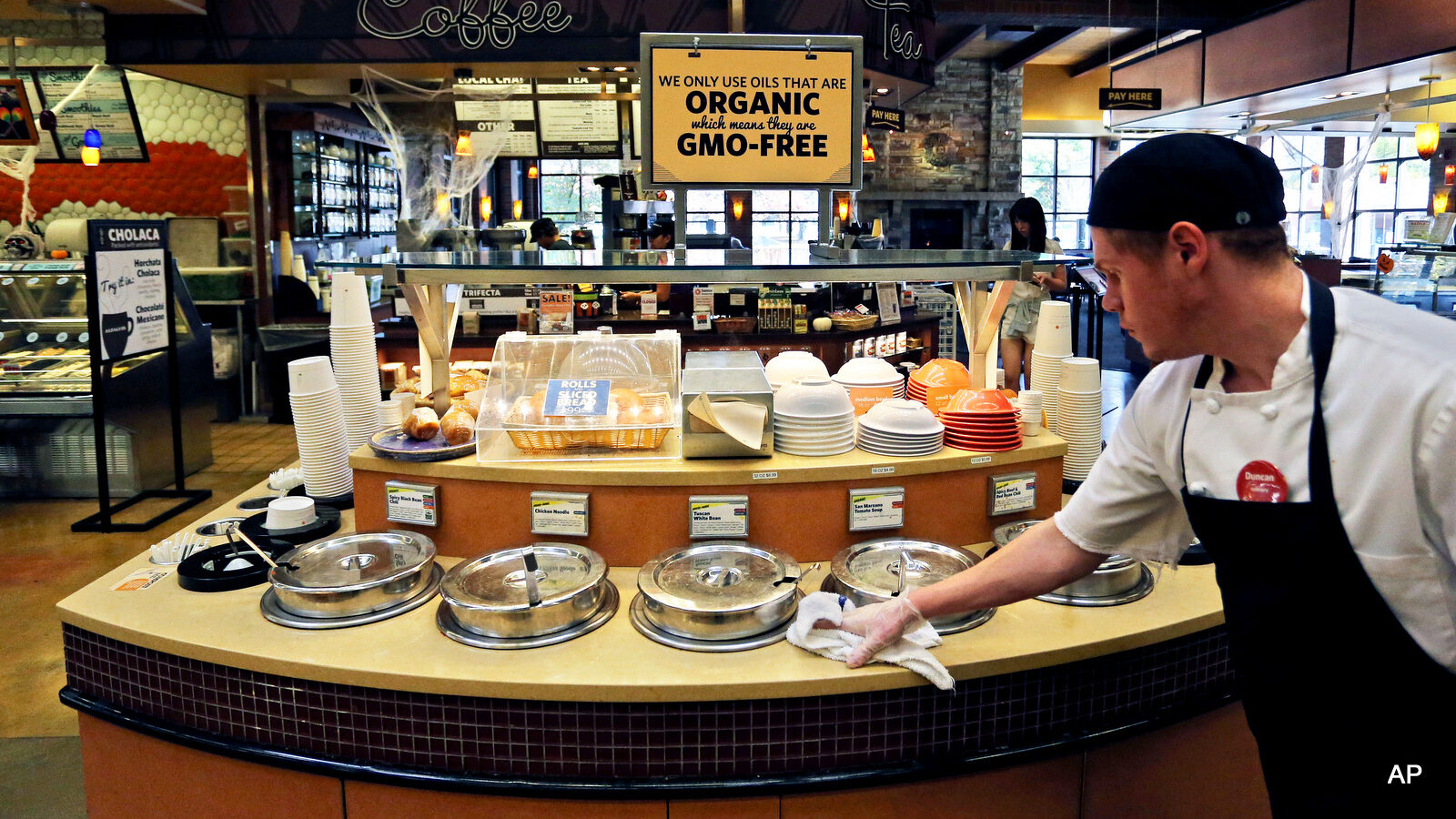 A grocery store employee wipes down a soup bar with a display informing customers of organic, GMO-free oils