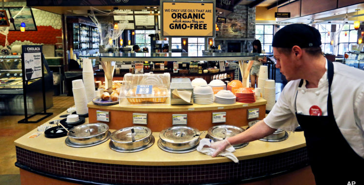 A grocery store employee wipes down a soup bar with a display informing customers of organic, GMO-free oils