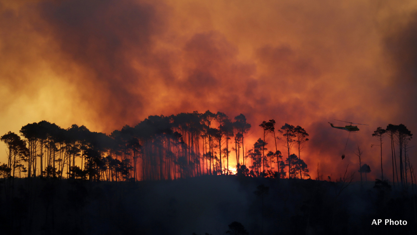 In this photo taken Monday, March 2, 2015, a helicopter water bombs fire in the Tokai Forest near Cape Town, South Africa. A wildfire continues to burn across the city's southern peninsula Tuesday, March 3, 2015 after breaking out Sunday with firefighting re-enforcements being flown in to assist with battling the blaze (AP Photo/Mark Wessels)