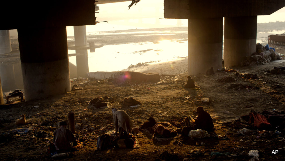 Homeless Indian men prepare themselves for the day ahead as they rise early morning by the banks of the River Yamuna in New Delhi, India.