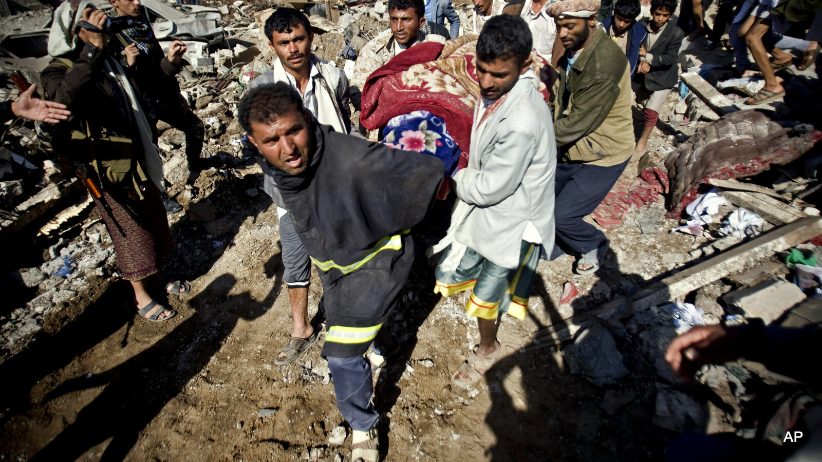 People carry the body of a woman covered with a blanket from under the rubble of houses destroyed by Saudi airstrikes near Sanaa Airport, Yemen, Thursday, March 26, 2015. Saudi Arabia launched airstrikes Thursday targeting military installations in Yemen held by Shiite rebels who were taking over a key port city in the country's south and had driven the embattled president to flee by sea, security officials said. (AP Photo/Hani Mohammed)