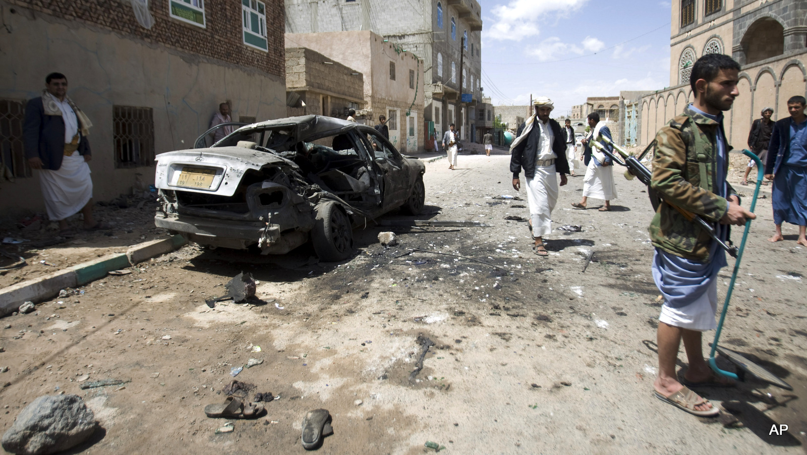 Houthis near a damaged car after a bomb attack in Sanaa, Yemen, Friday, March 20, 2015.