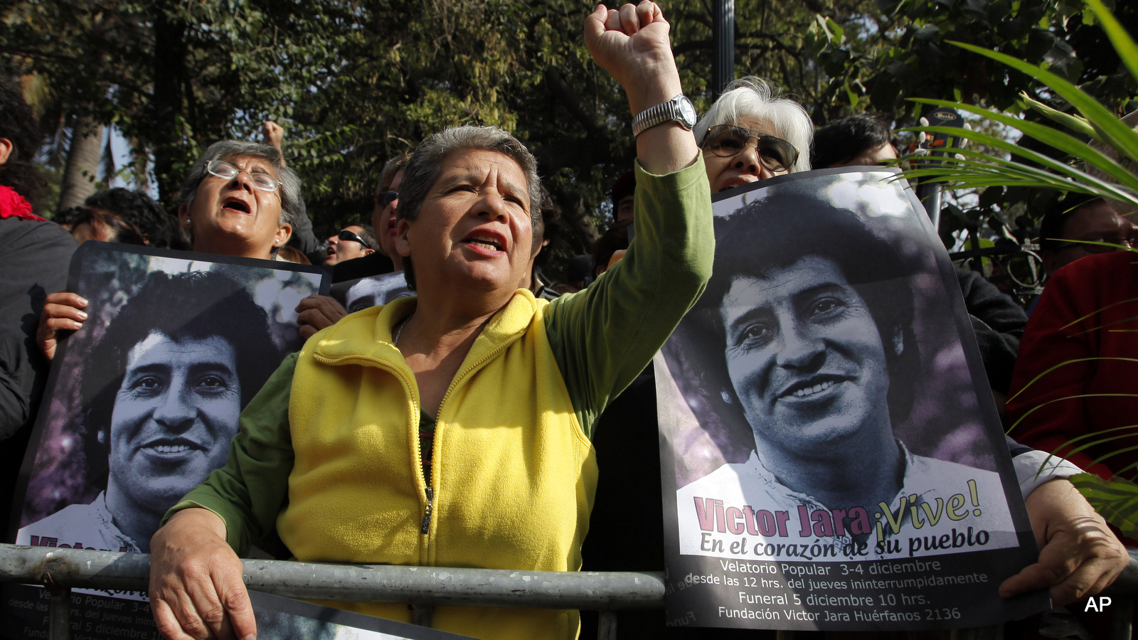 A woman gestures to the passing coffin of Chile's folk singer Victor Jara as others hold posters of him during his funeral procession in Santiago, Saturday, Dec. 5, 2009.  Jara's burial comes 36 years after he was beaten and shot by soldiers in a stadium where the military gathered thousands of arrested supporters of ousted president Salvador Allende in the days following the 1973 military coup led by Gen. Augusto Pinochet.  Jara's body was exhumed six months ago for a proper autopsy as part of an ongoing investigation to determine the circumstances of his death.