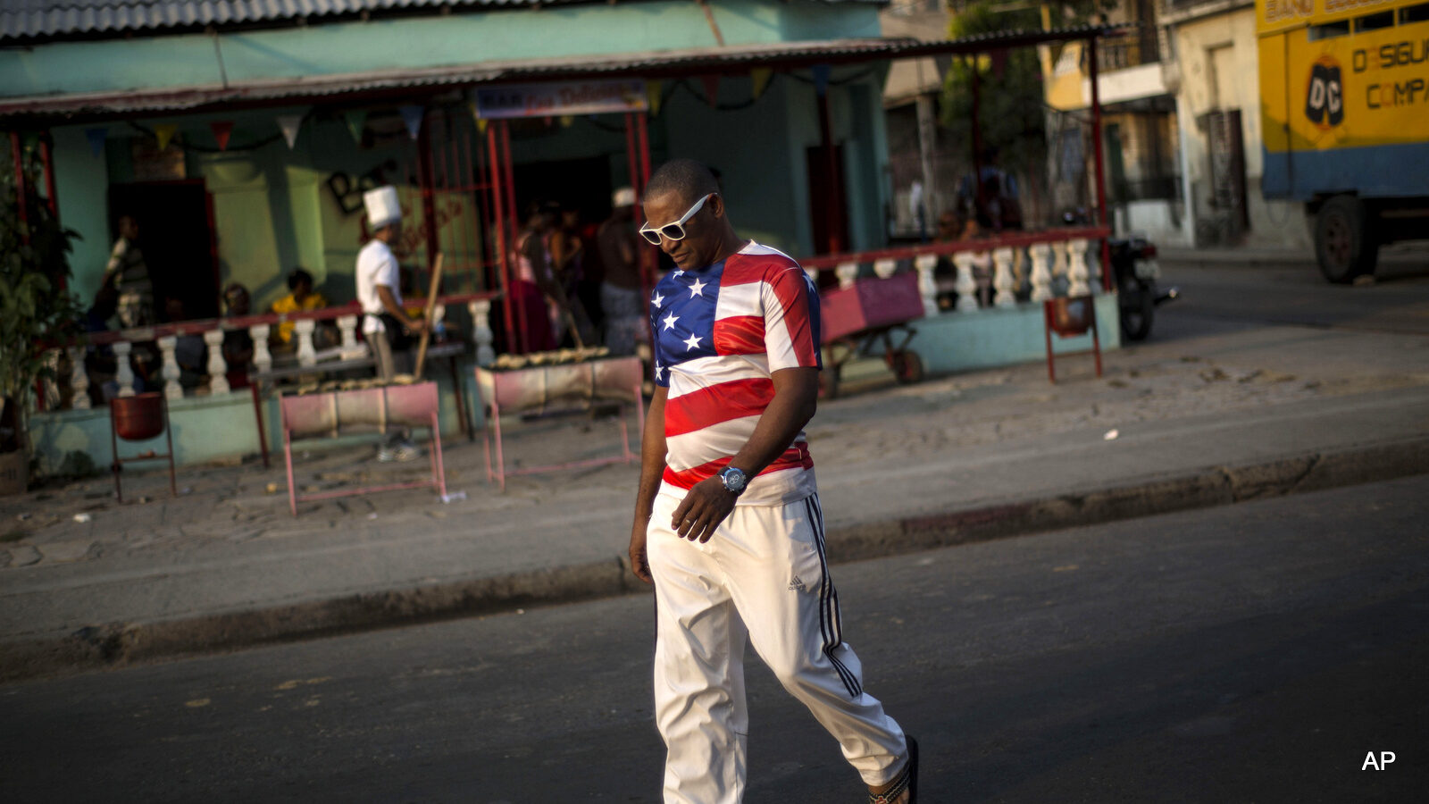 A man wears a shirt with a U.S. flag design in Santiago, Cuba. It’s easier to get from Havana to Miami than to the island’s second-largest city, which has just two overbooked flights a day and trains that are achingly slow and unpredictable. )