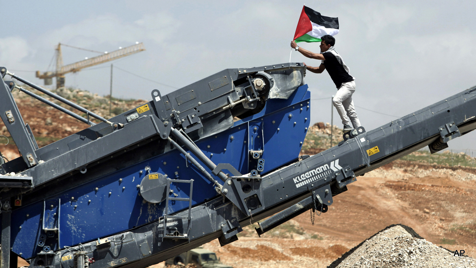 A protester posts a Palestinian flag on Israeli construction equipment at a building site adjacent to the Israeli settlement of Beitar Illit during a protest marking Land Day, in the village of Wadi Fukin, near the West Bank city of Bethlehem, Monday, March 30, 2015. Land Day commemorates riots on March 30, 1976, when six people were killed during a protest by Israeli Arabs whose property was annexed in northern Israel to expand Jewish communities.