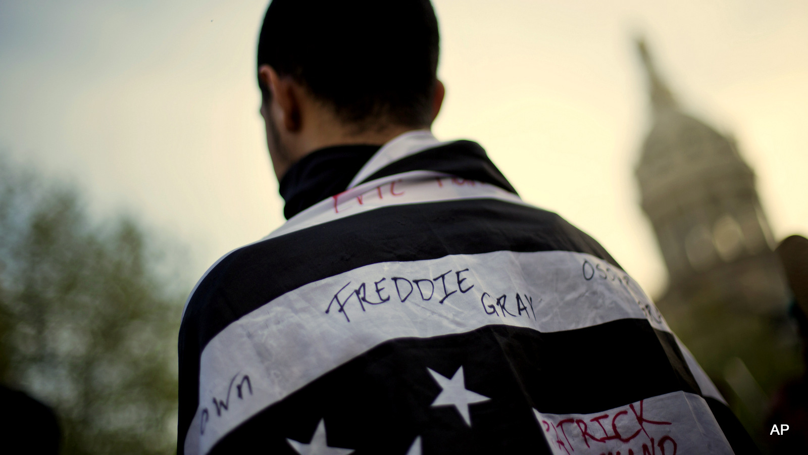 A protestor wears a flag decorated with the name of Freddie Gray during a demonstration outside City Hall, Wednesday, April 29, 2015, in Baltimore. 