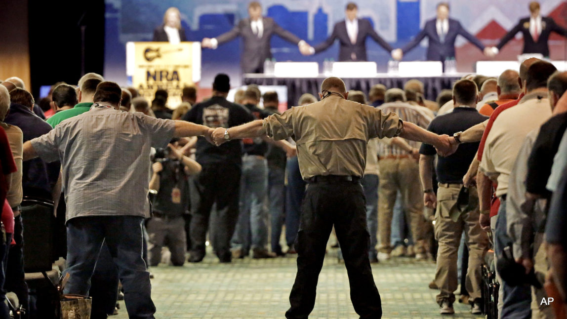 National Rifle Association members hold hands during the opening prayer at the annual meeting of members at the NRA convention Saturday, April 11, 2015, in Nashville, Tenn.
