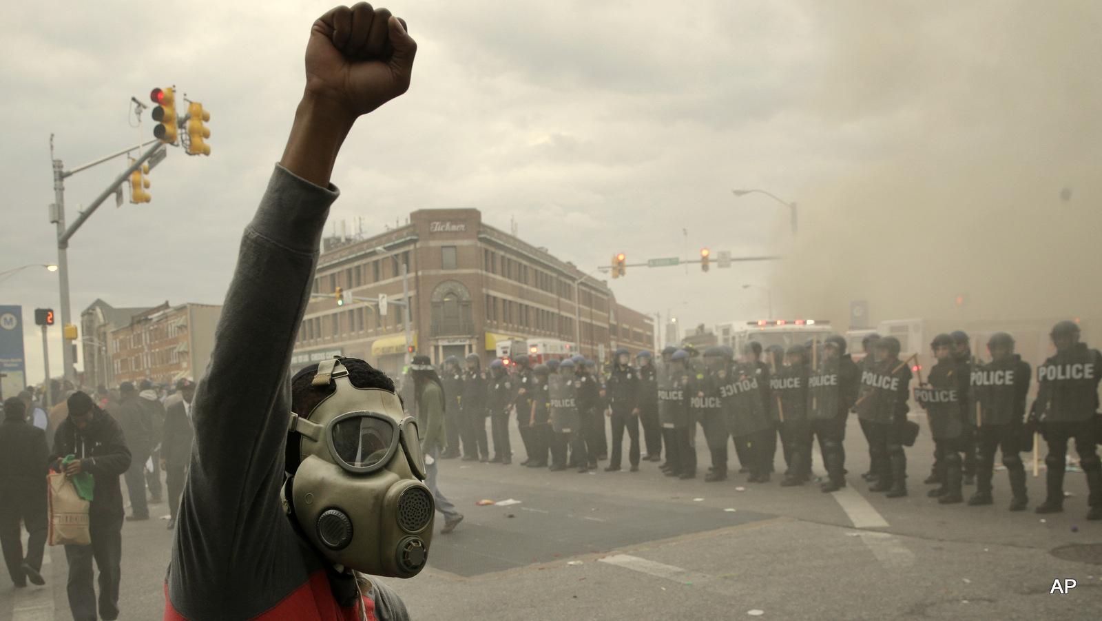 A demonstrator raises his fist as police stand in formation as a store burns, Monday, April 27, 2015, during unrest following the funeral of Freddie Gray in Baltimore. 