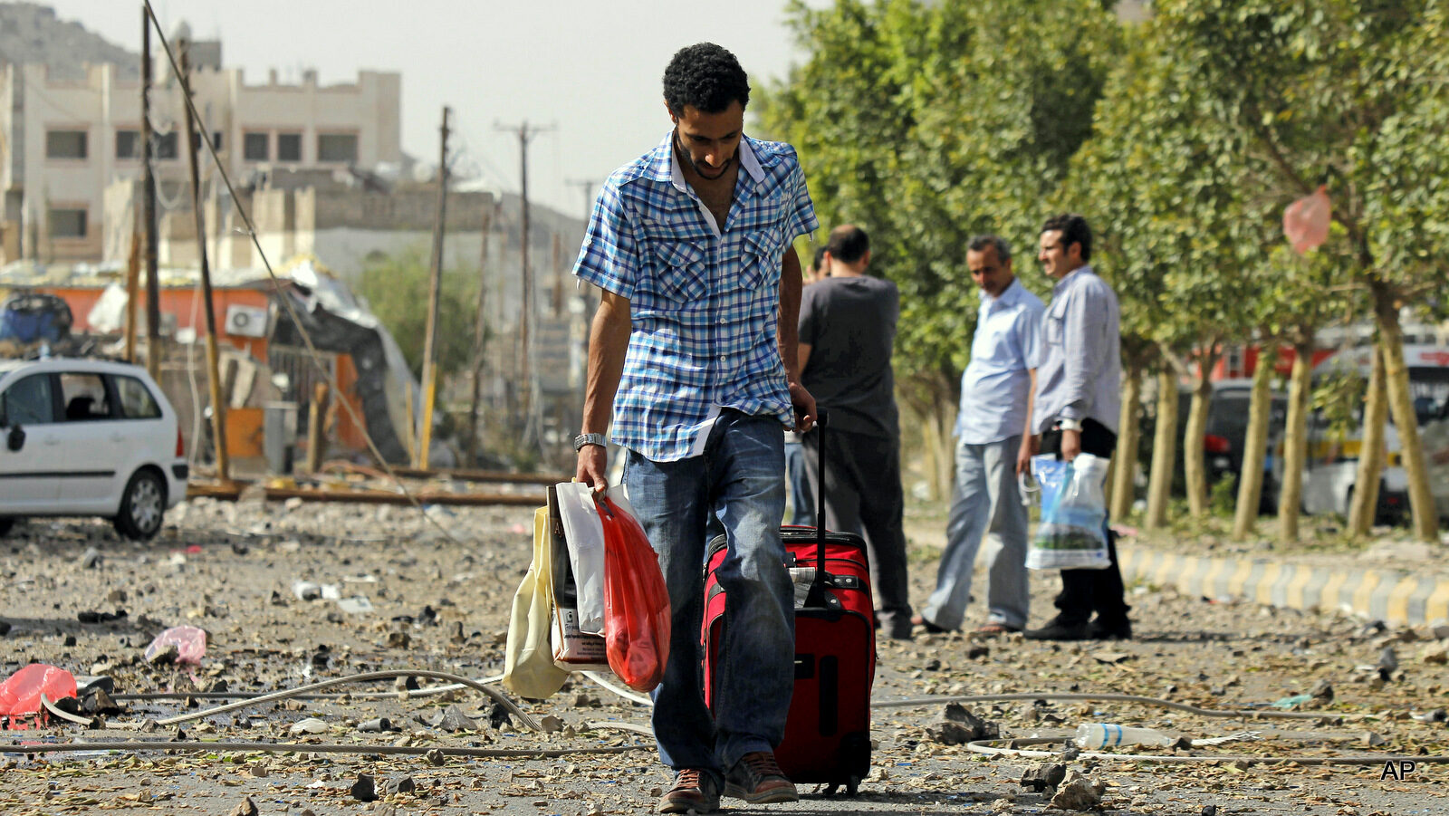 A man carries his belongings on a street littered with debris as he flees from his home after a Saudi-led airstrike against the Houthis, that hit a site of an alleged weapons cache in Yemen's capital, Monday, April 20, 2015. Saudi-led airstrikes caused massive explosions that shattered windows, sent residents scrambling for shelter and killed a local TV presenter.