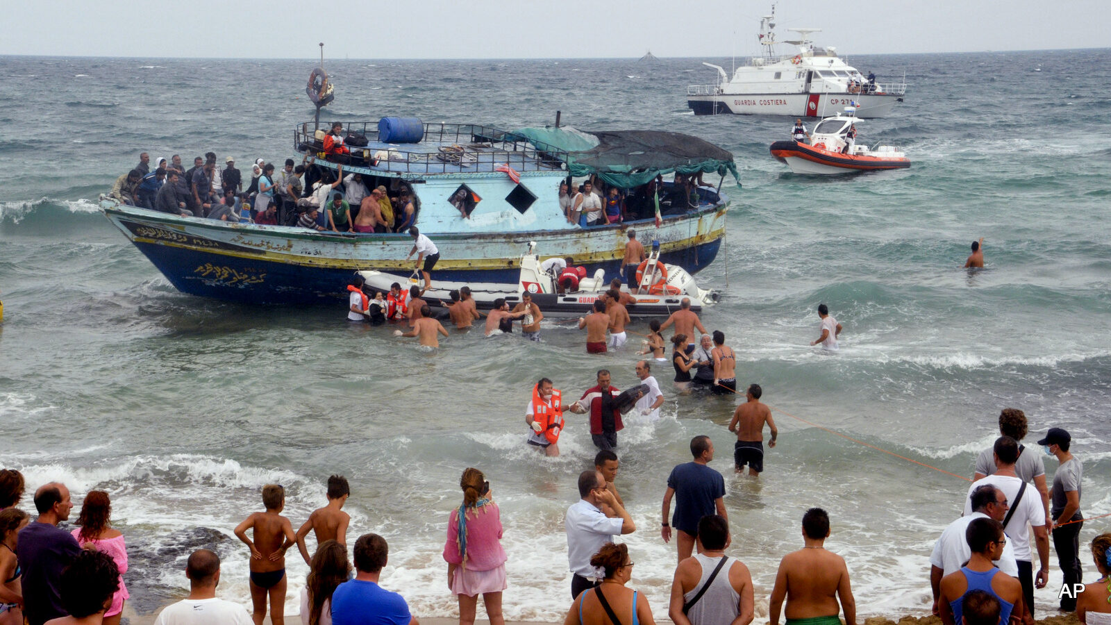 Italian Coast Guard officers and holiday-makers help migrants to get off a boat near Siracusa, Italy.