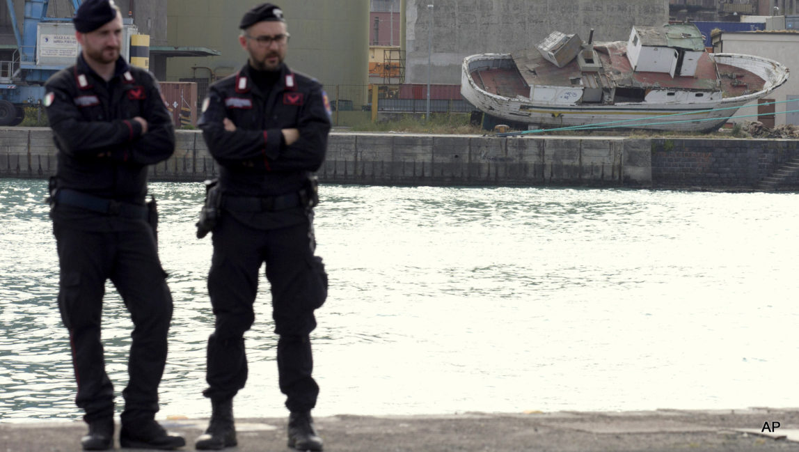 Italian forces stand guard in front of the wreckage of a boat used by migrants in Catania's Harbour, Italy, Monday, April 20, 2015.
