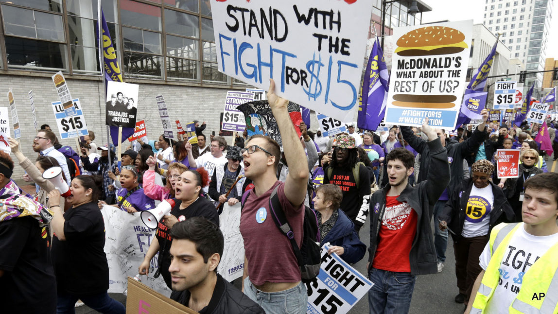 Boston University student Patrick Johnson, center, holds a sign as he joins with other protesters, including students, fast-food restaurant employees and other workers, as they march Tuesday, April 14, 2015, in Boston.
