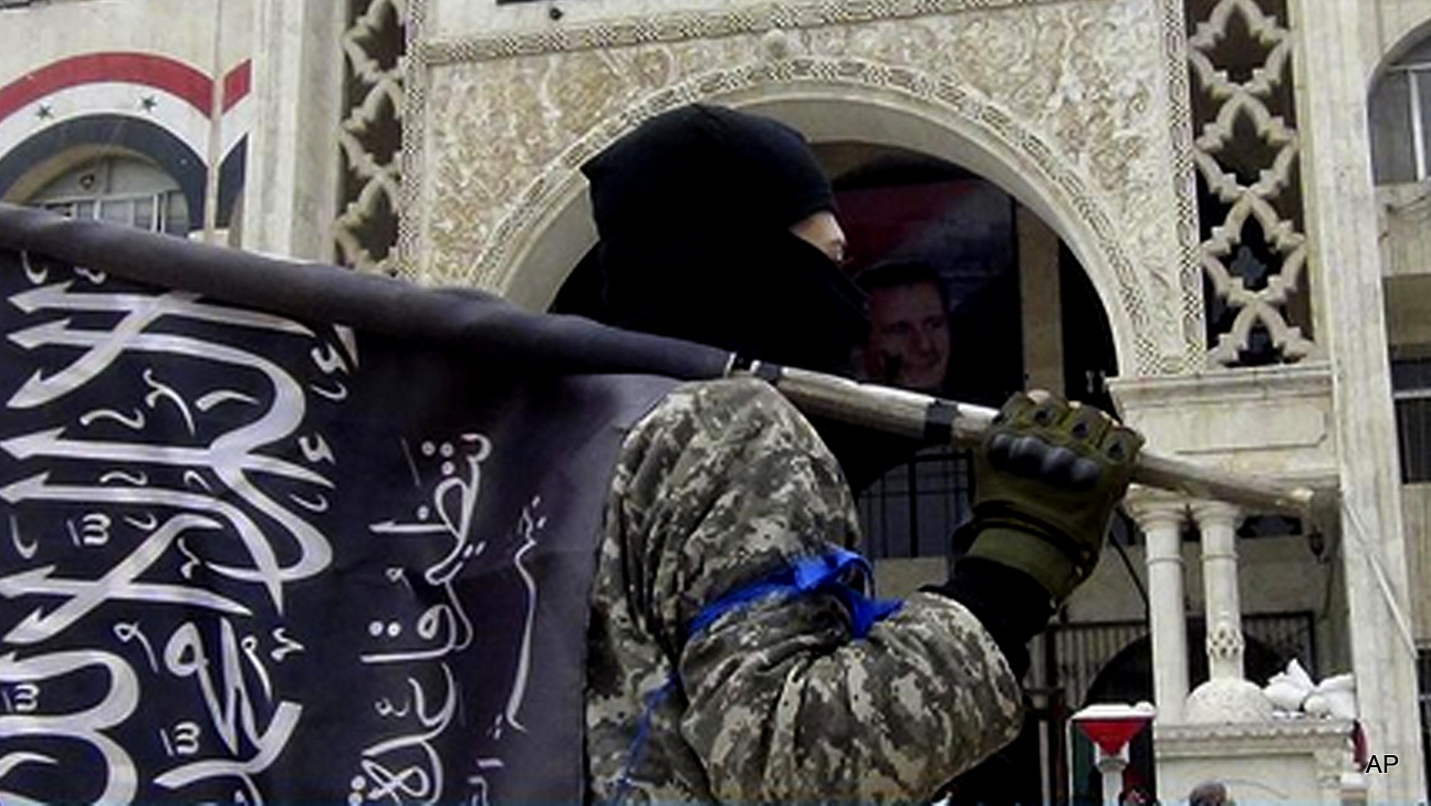 A fighter from Syria's al-Qaida-linked Nusra Front holds his group flag as he stands in front of the governor building in Idlib province, north Syria. 